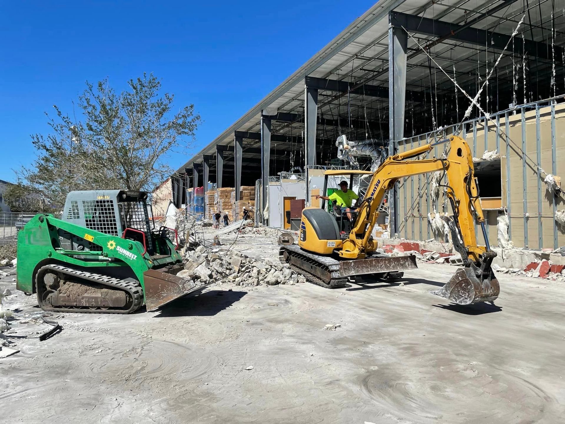 A large yellow excavator is demolishing a building