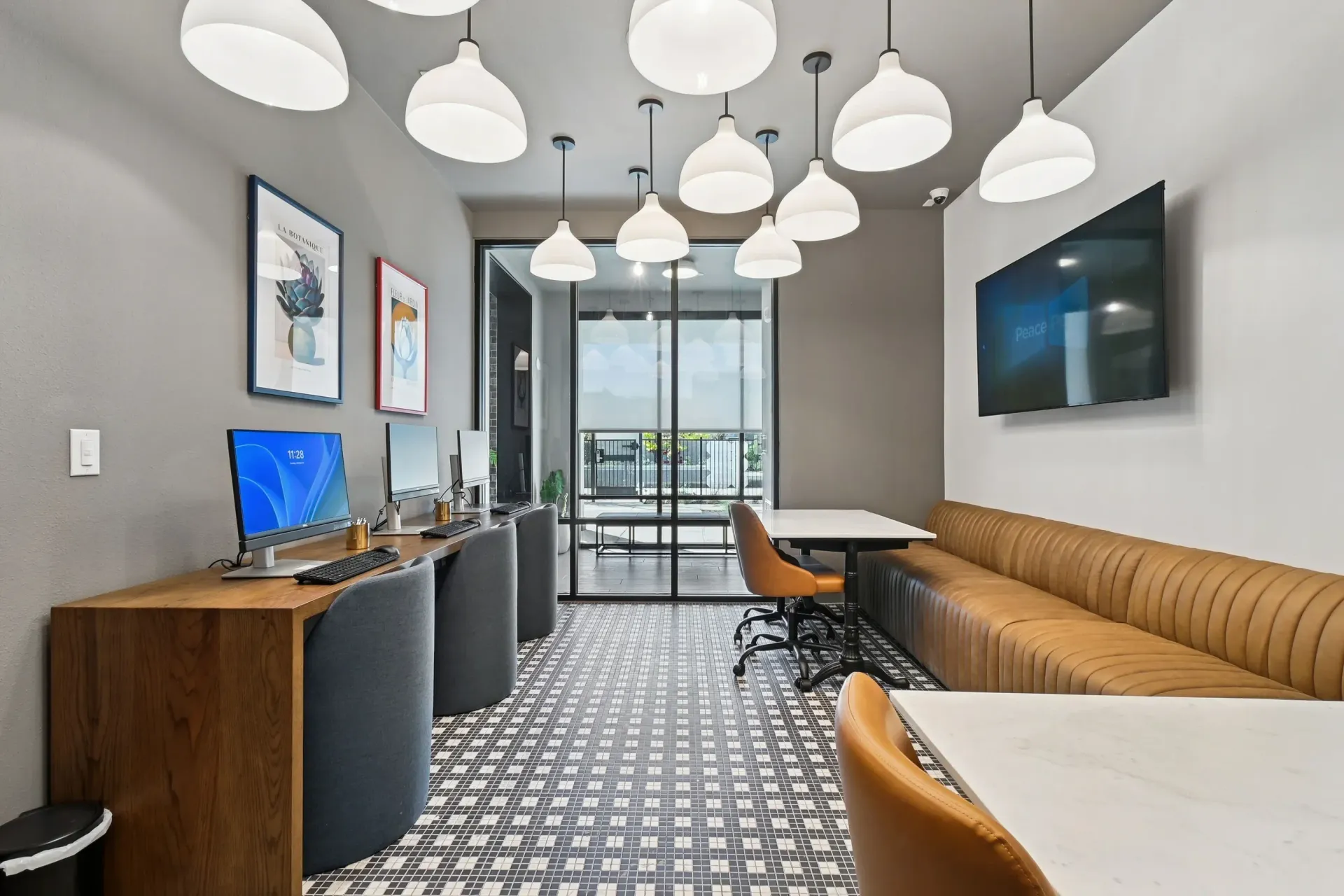 Contemporary community lounge with computer stations, seating, and a wall-mounted TV at Ennova Highlands apartments in Arlington, TX.