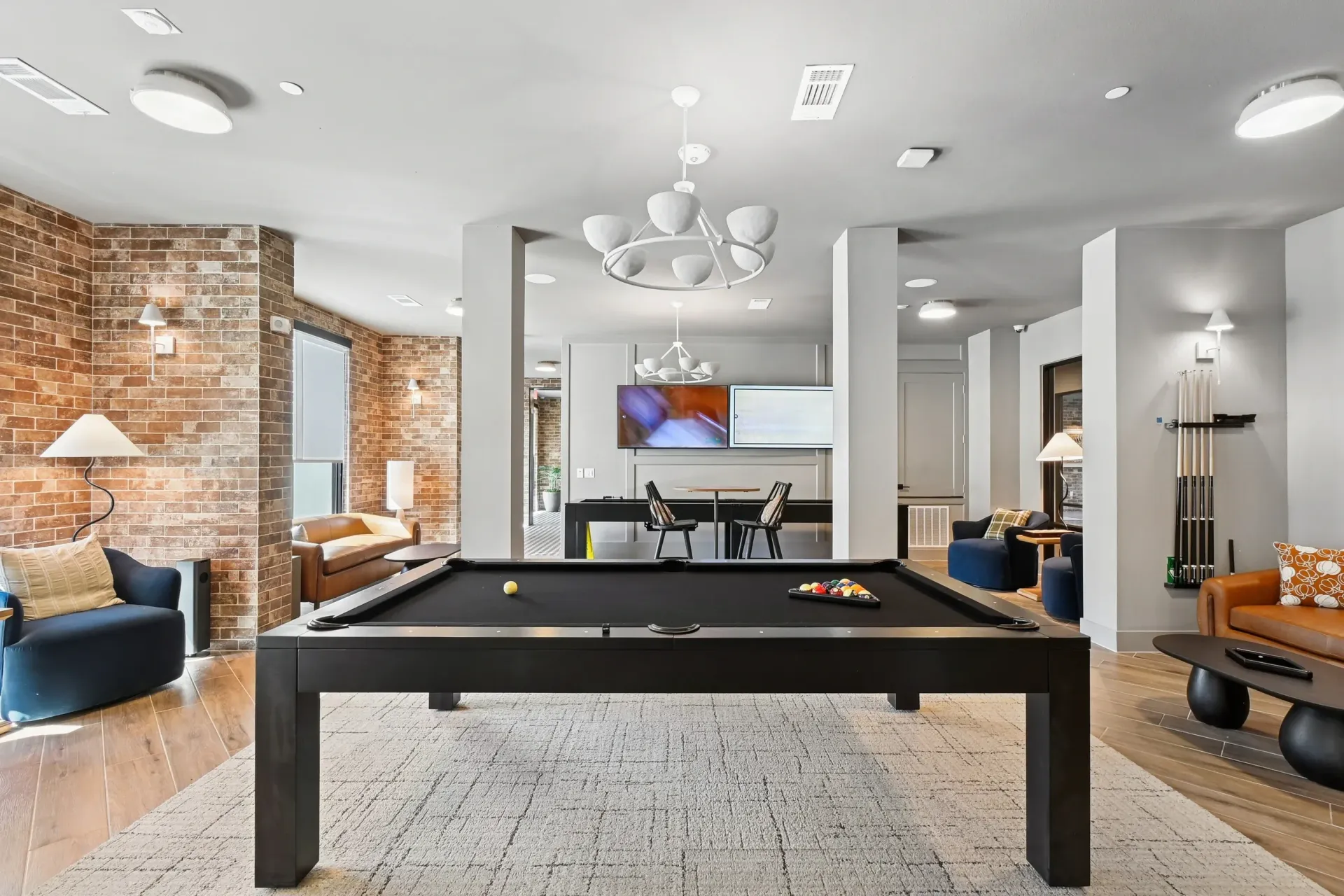Interior community lounge with a pool table, brick accent walls, and seating at Ennova Highlands apartments in Arlington, TX.