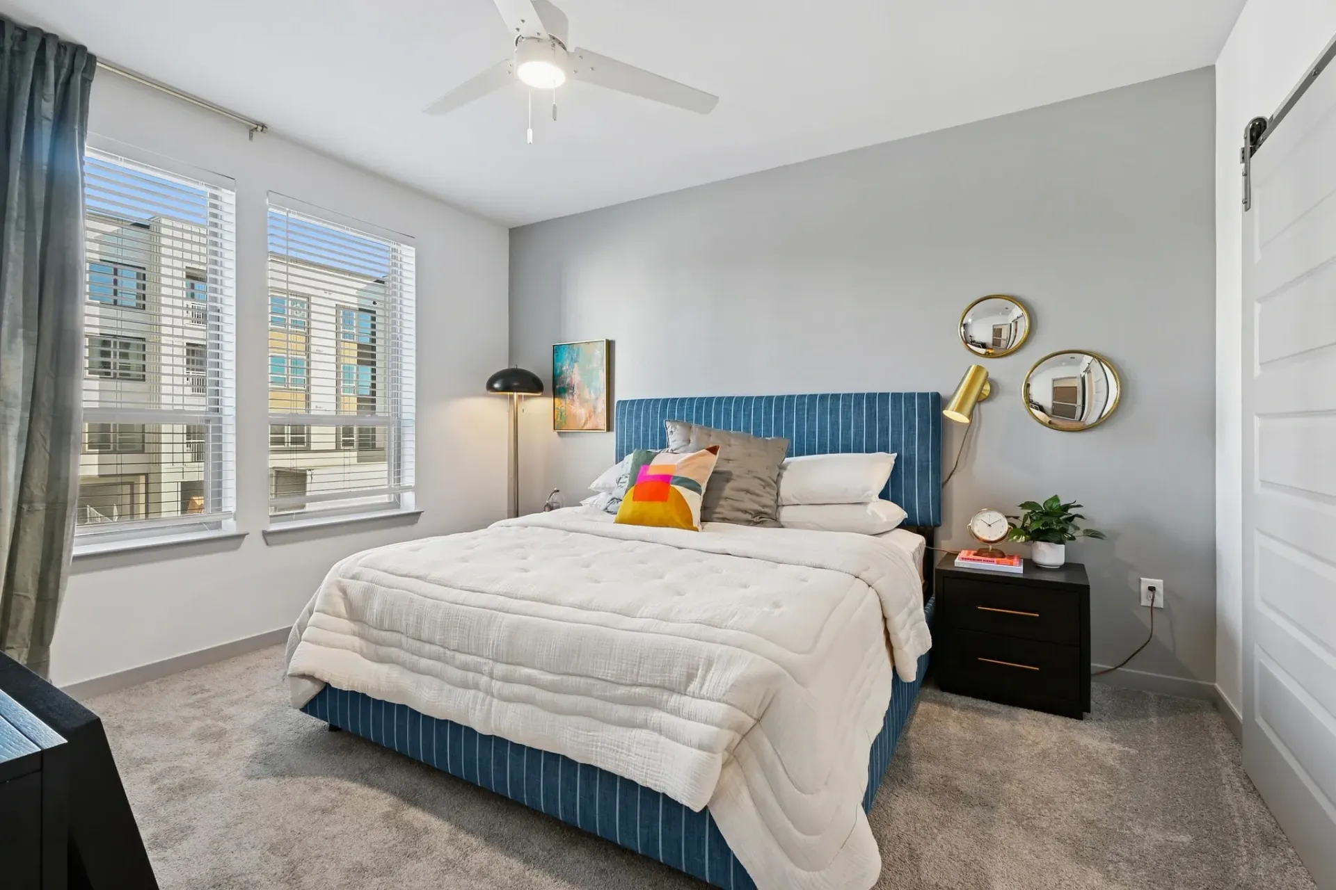 Bedroom in an apartment with a blue upholstered bed, white bedding, gray walls, and two large windows at Ennova Highlands apartments in Arlington, TX.