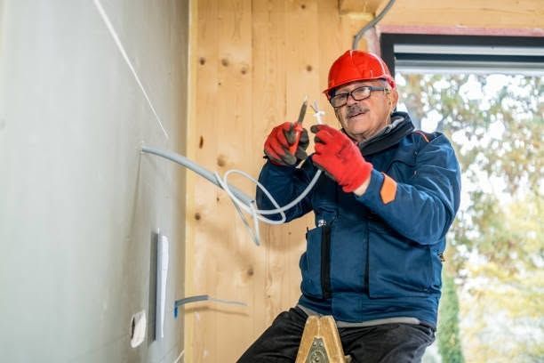 Worker in red hard hat wiring an outlet inside a partially finished room. Worker in red hard hat wiring an outlet inside a partially finished room.