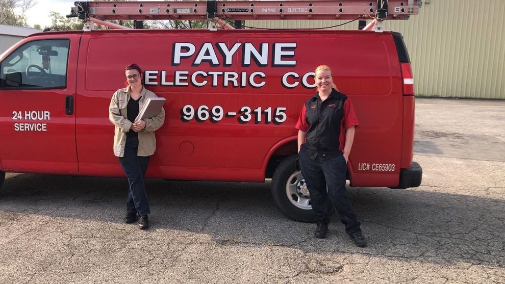 Two people standing beside a red Payne Electric Co. service van in a gravel lot Two people standing beside a red Payne Electric Co. service van in a gravel lot