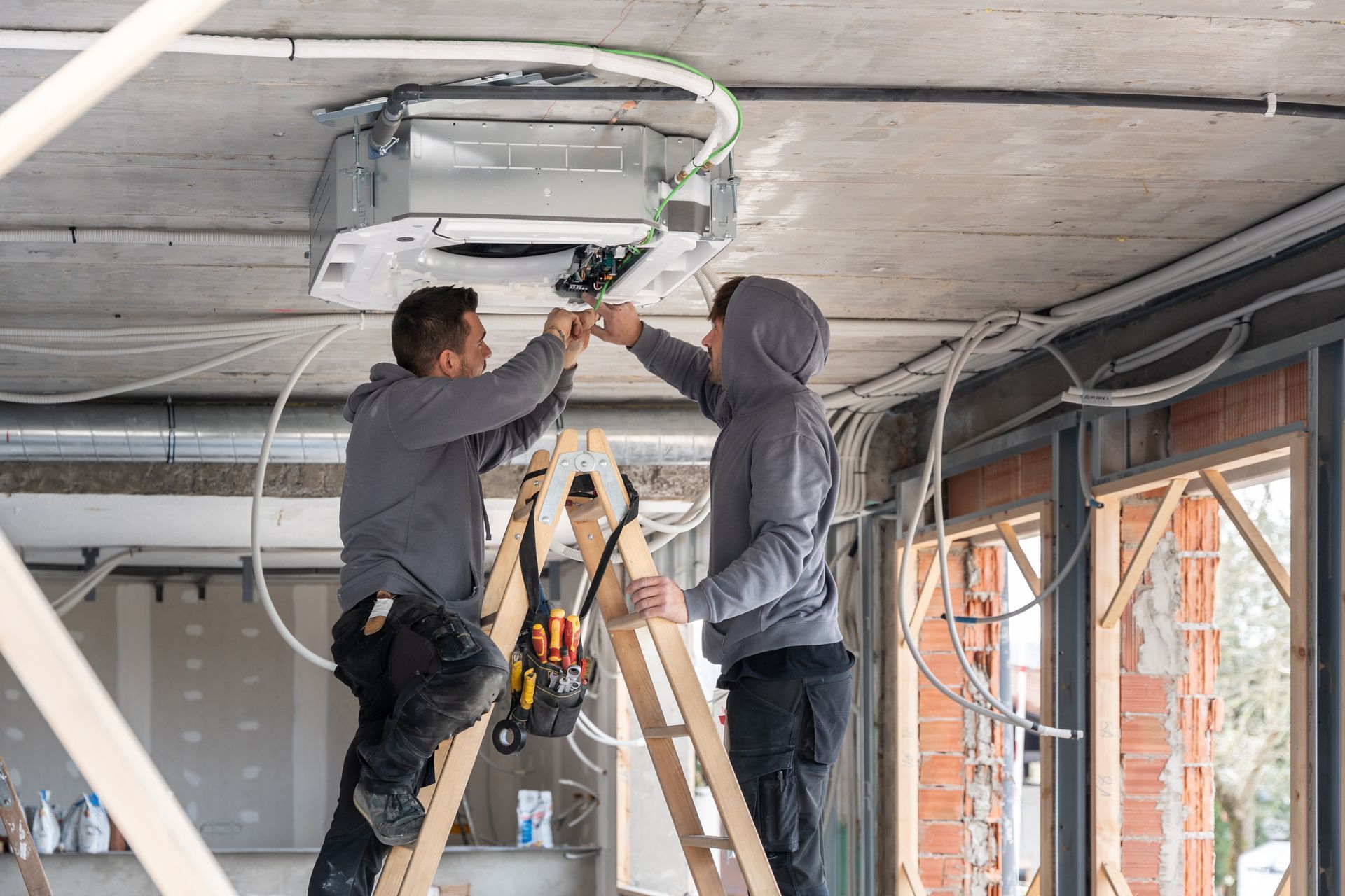 Two workers installing a ceiling-mounted air conditioner in a room under construction. Two workers installing a ceiling-mounted air conditioner in a room under construction.