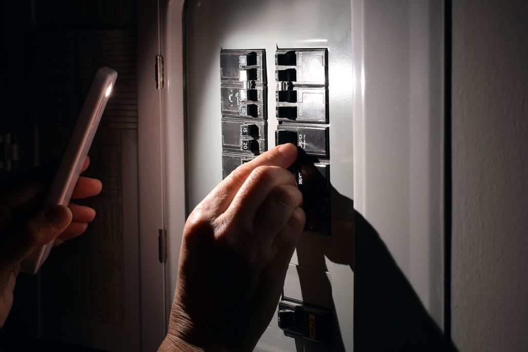 Hands turning on a wall breaker panel with a flashlight nearby, in a dim room Hands turning on a wall breaker panel with a flashlight nearby, in a dim room