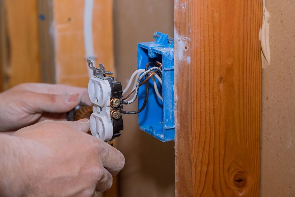 Hands wiring a white electrical outlet into a blue wall box beside wood paneling. Hands wiring a white electrical outlet into a blue wall box beside wood paneling.
