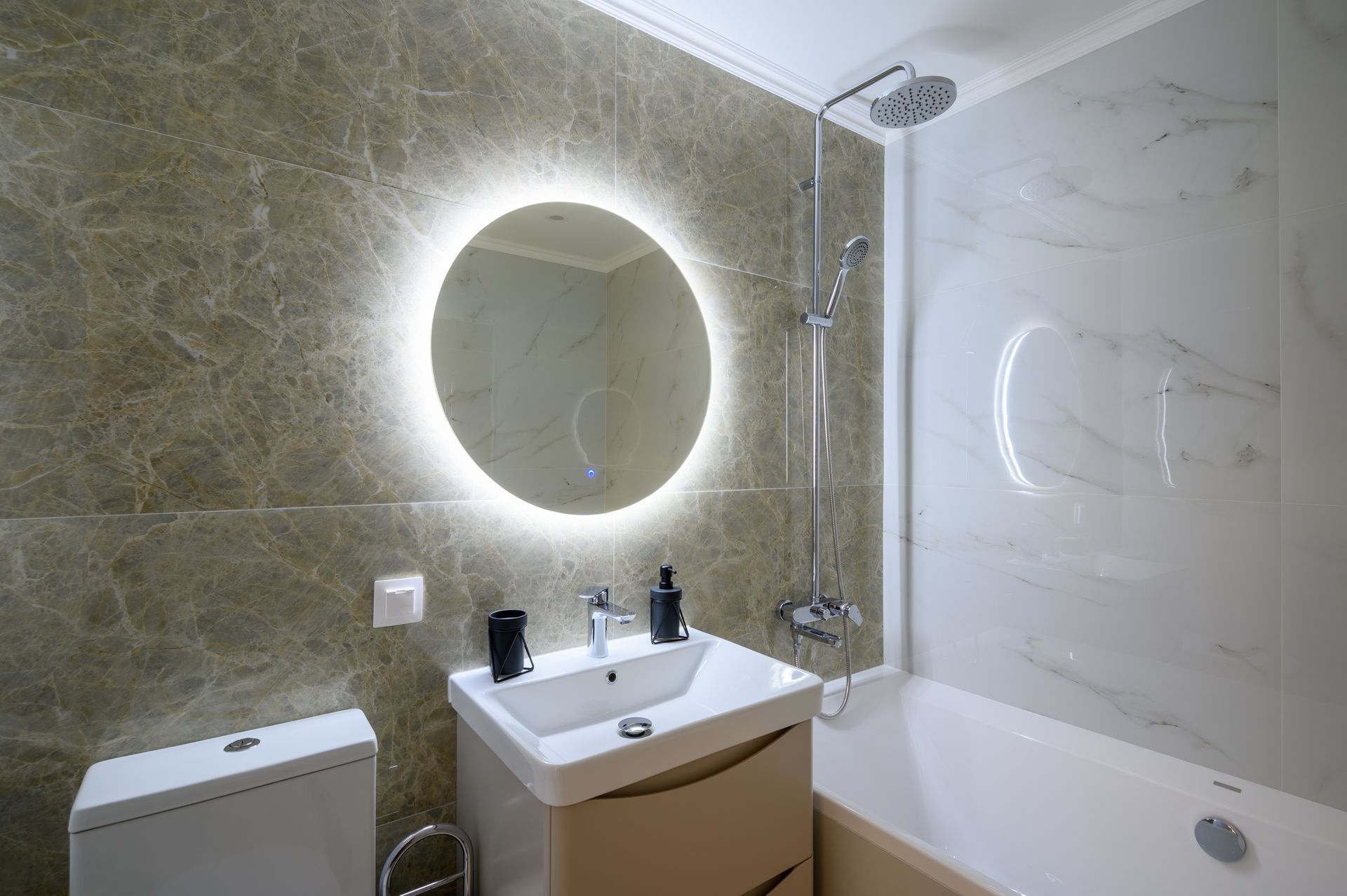 Modern bathroom with lit round mirror, sink, toilet, and bathtub with shower panel