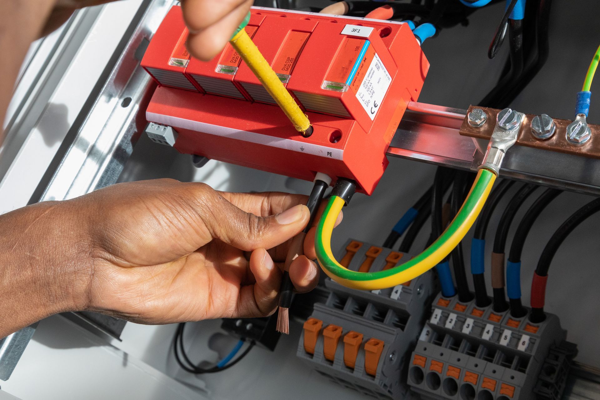 Hands wiring a yellow-green grounding cable in an electrical panel with a red tool and terminal blocks. Hands wiring a yellow-green grounding cable in an electrical panel with a red tool and terminal blocks.