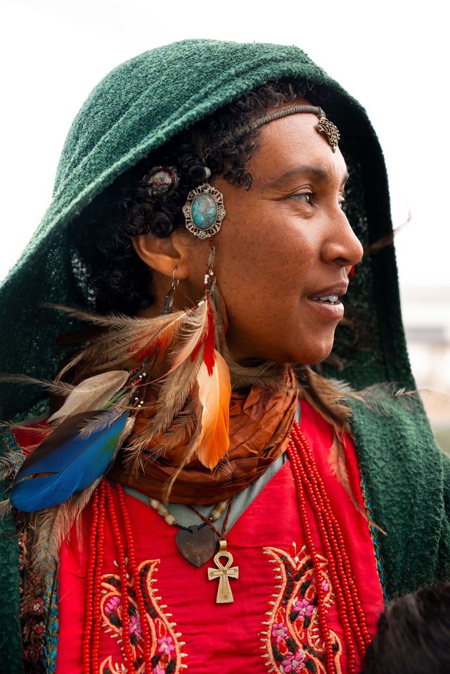 A woman wearing a green hood and feathers on her head.
