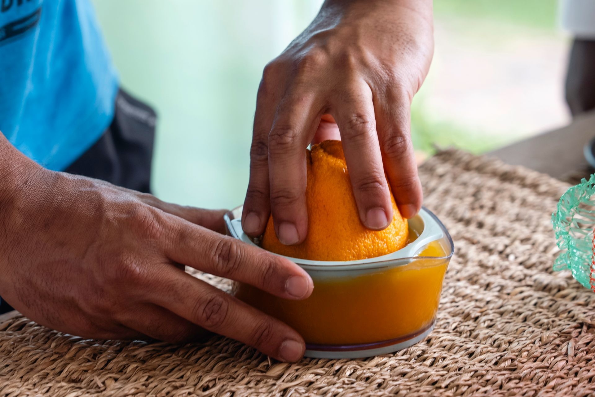 A man is squeezing an orange into a bowl of orange juice.