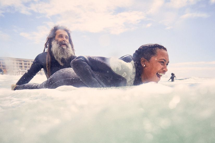 A man and a woman are laying on a surfboard in the ocean.