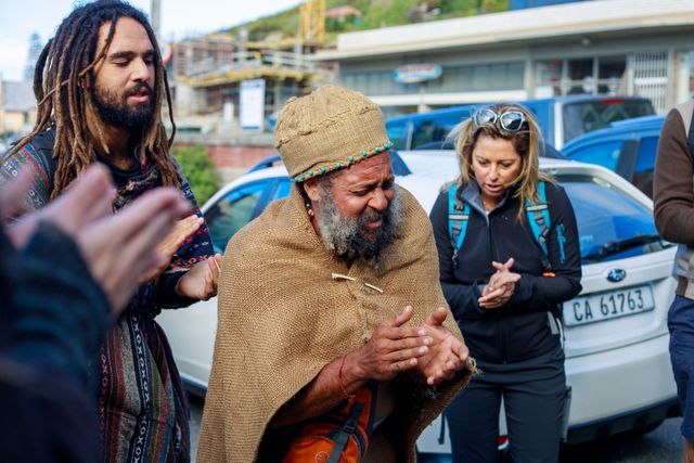 A man with dreadlocks and a beard is standing in front of a group of people.