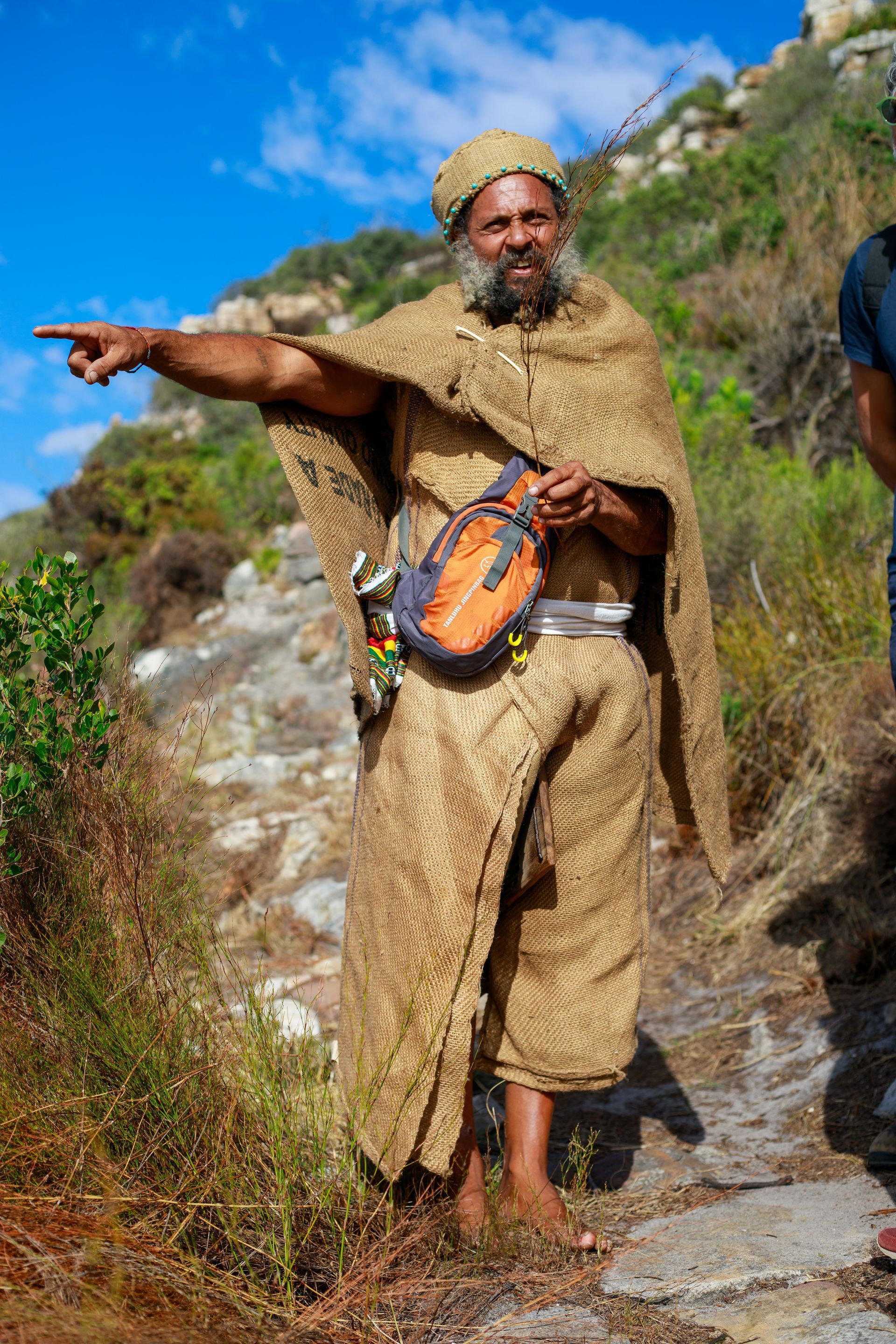 A man with a beard is wearing a poncho and pointing at something.