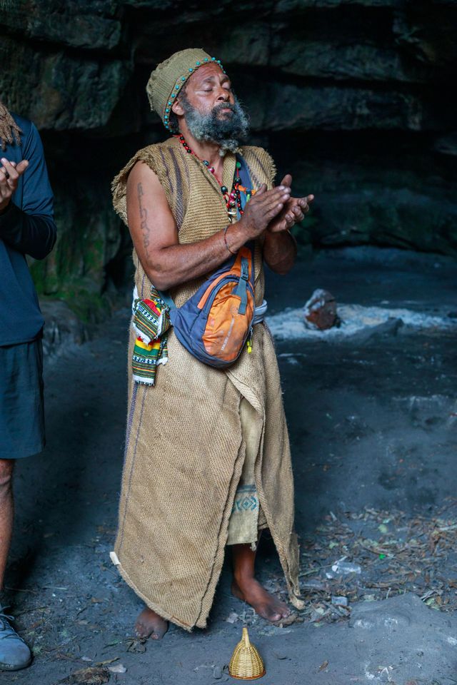 A man with a beard is praying in a cave.