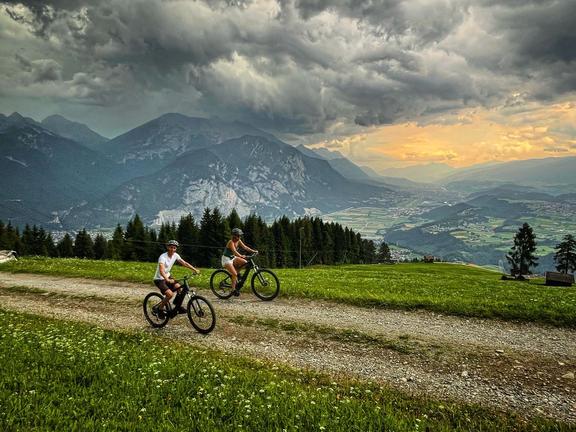 Two people are riding bicycles down a dirt road in the mountains.