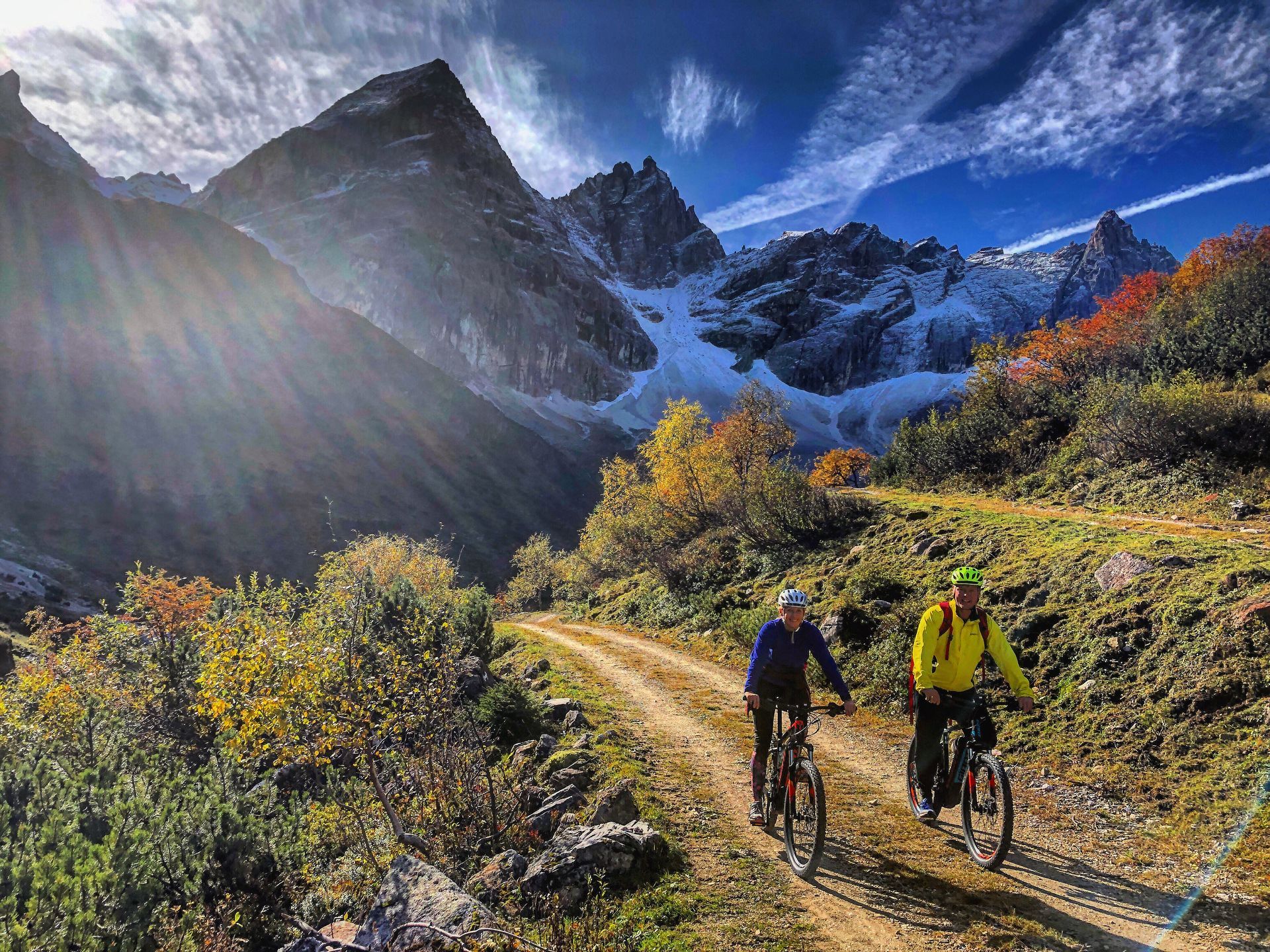Two people are riding bicycles down a dirt road in the mountains.