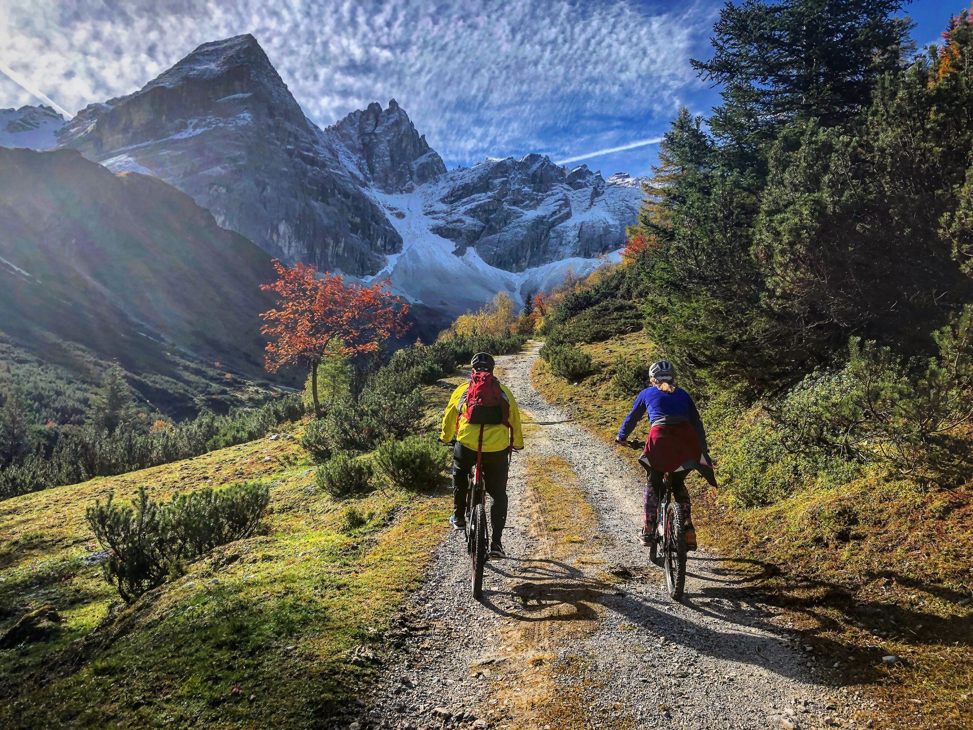Two people are riding bicycles down a dirt road in the mountains.