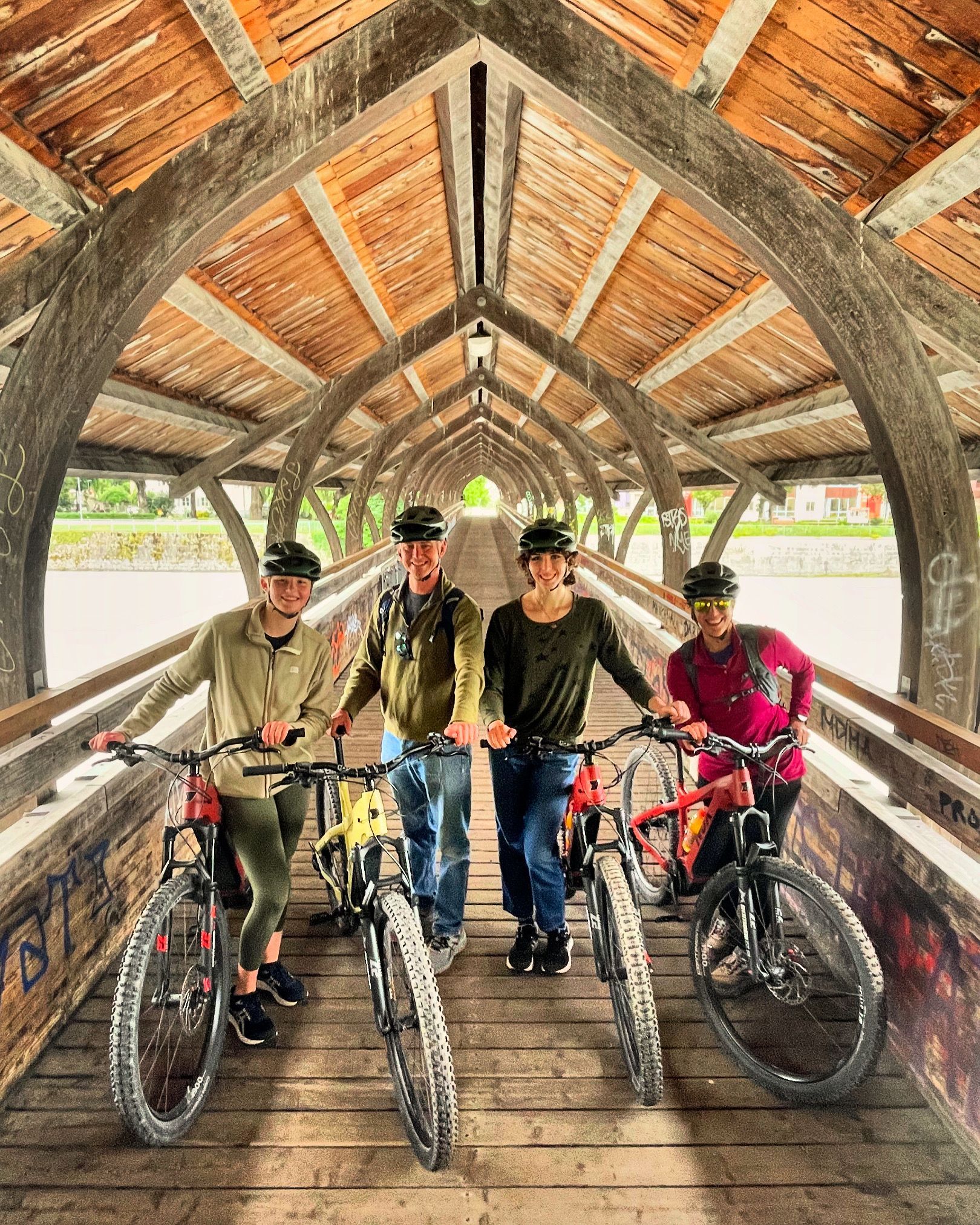 A group of people are standing on a wooden bridge with their bicycles.