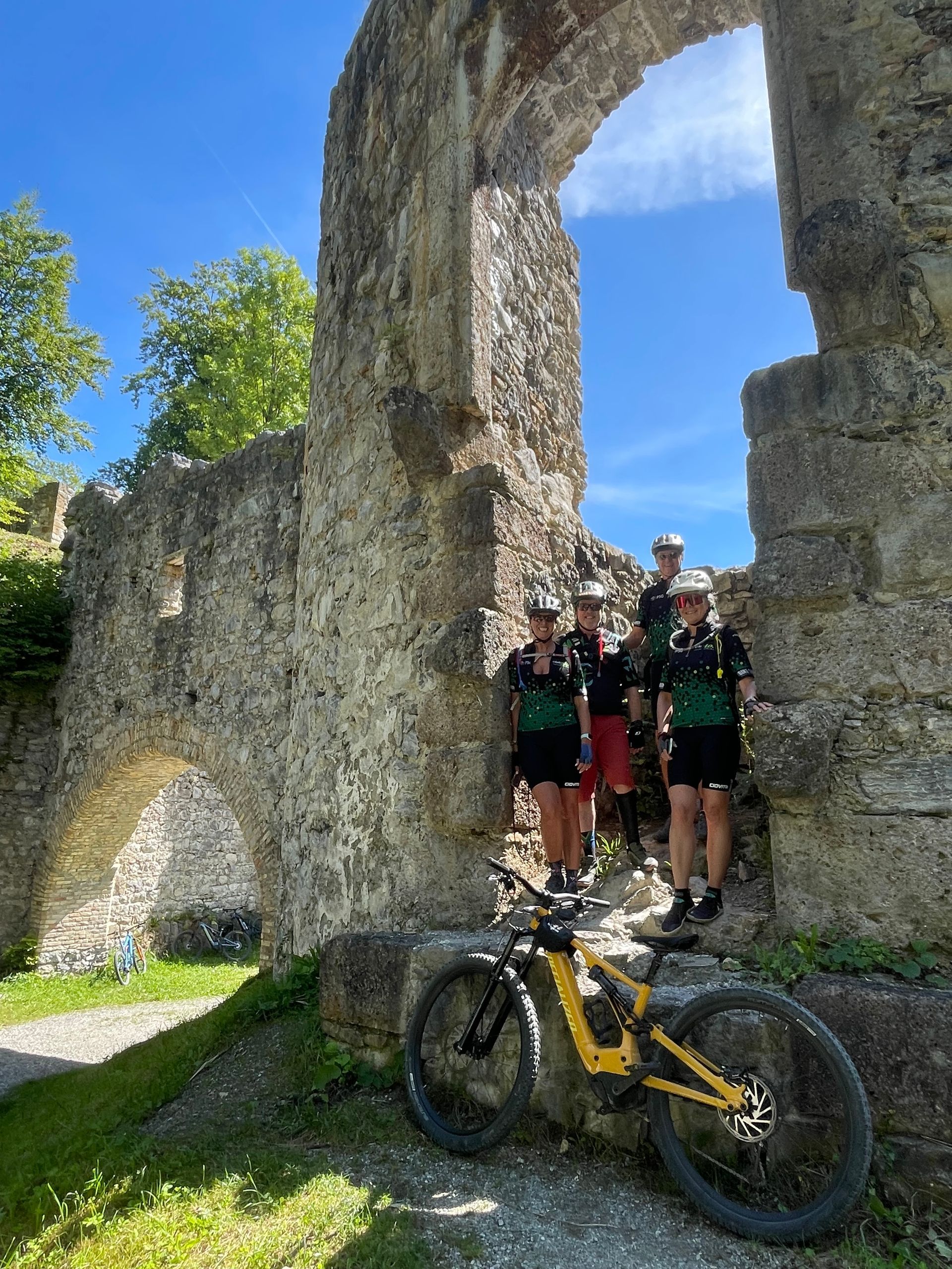 A group of people standing next to a bicycle in front of a stone wall.