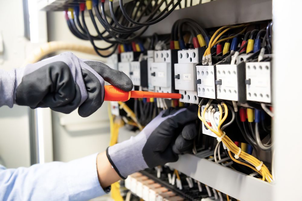 A person is working on an electrical box with a wrench.