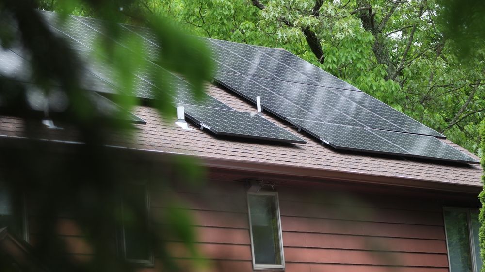 A house with solar panels on the roof is surrounded by trees.