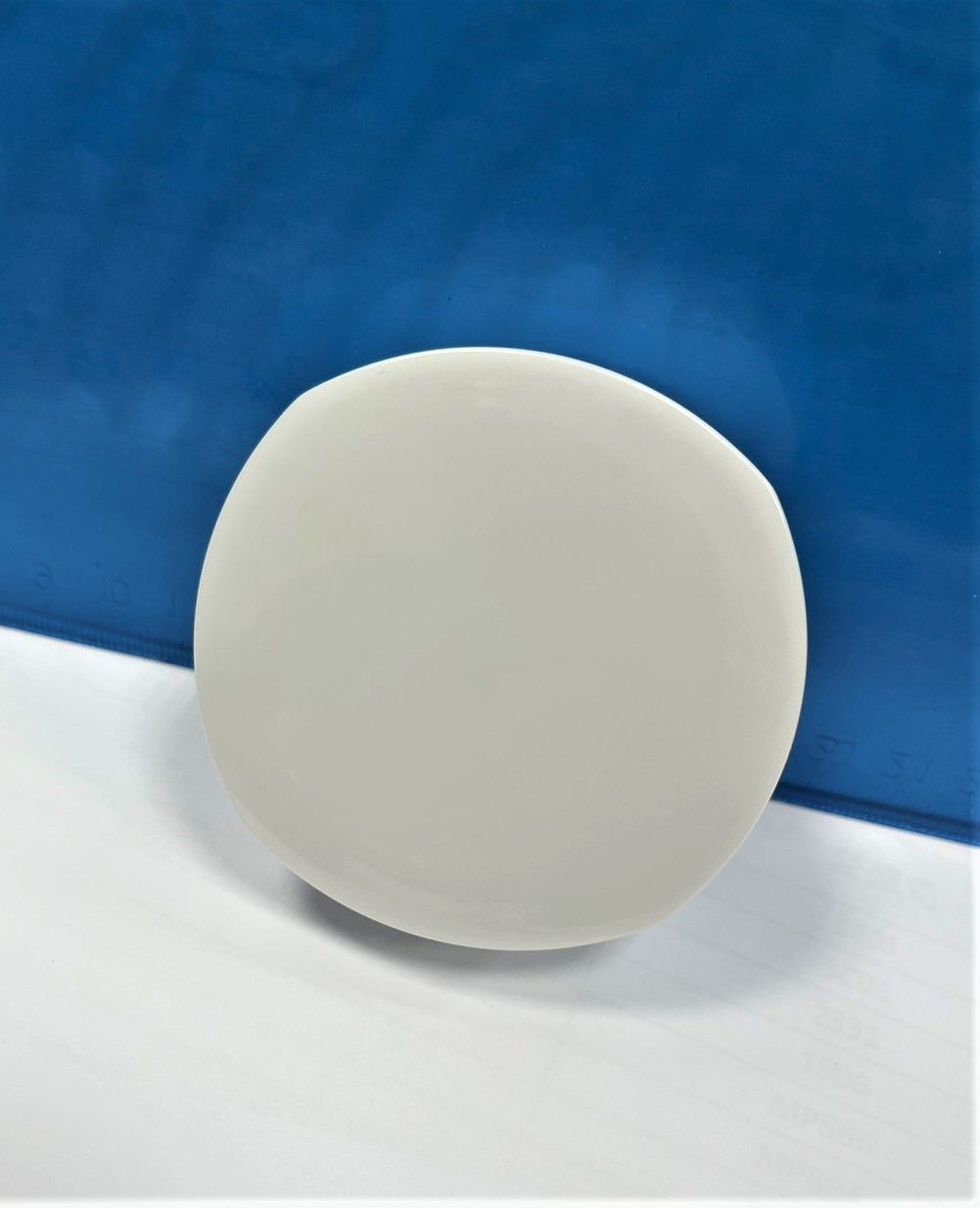 A white circle is sitting on a white surface in front of a blue background.