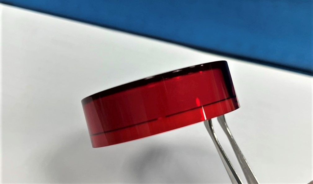 A red object is being held by tweezers on a white surface.