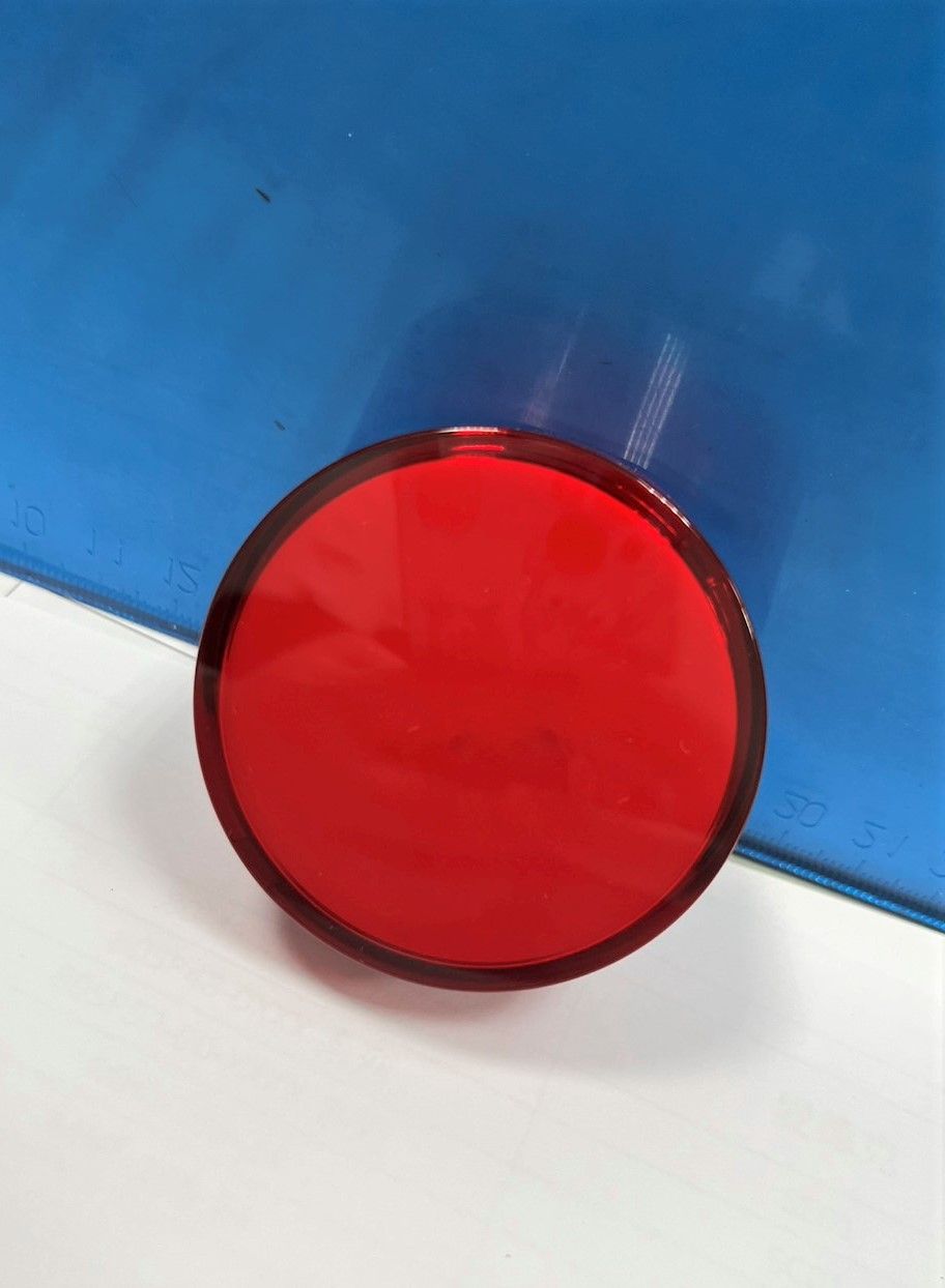 A red button is sitting on a white surface.