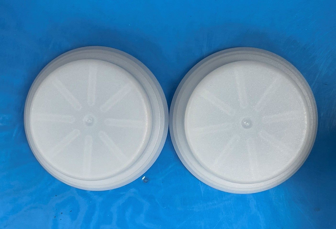 Two white plastic lids are sitting on a blue surface.