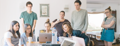 A group of people are sitting around a table looking at a laptop.