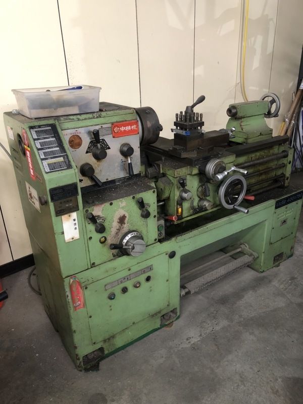 A green lathe is sitting in a garage next to a wall.