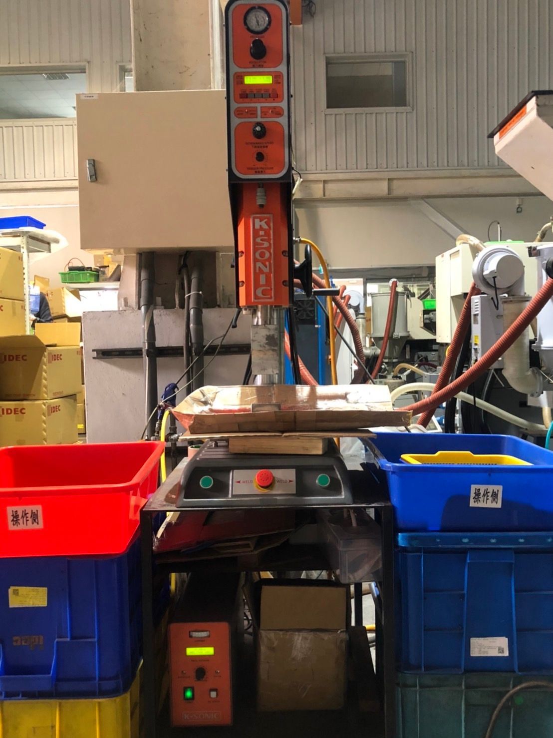 A machine is sitting on a table in a factory surrounded by blue and red bins