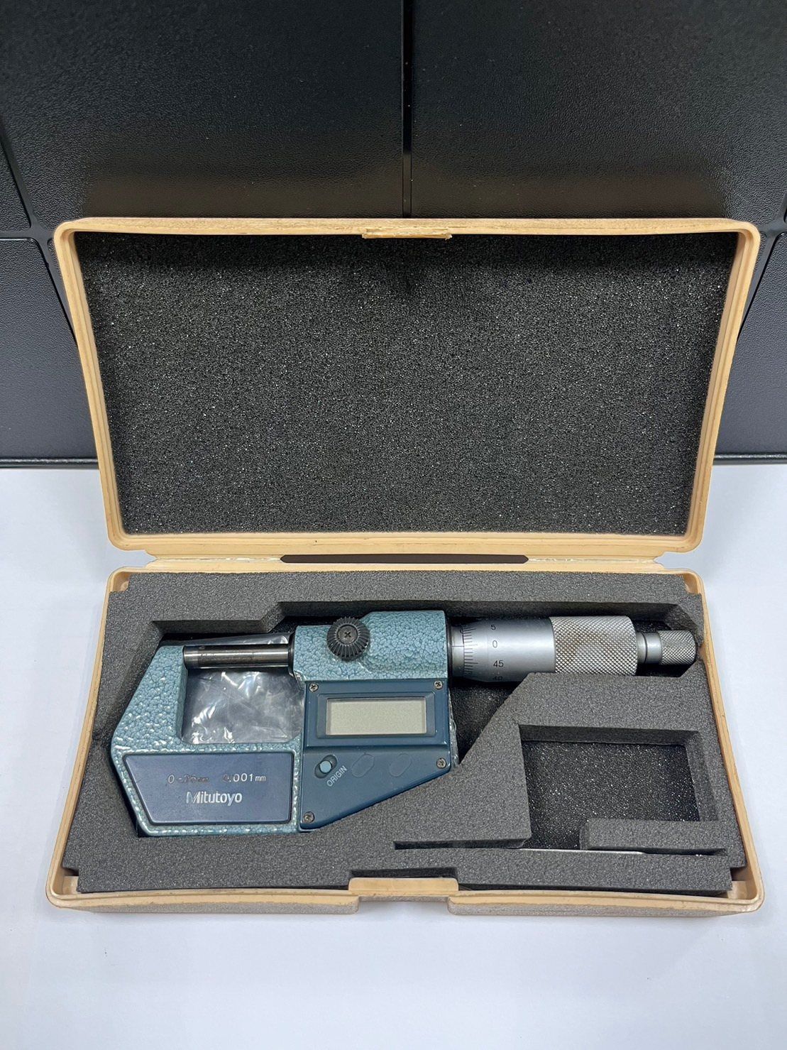 A digital micrometer is in a box on a table.