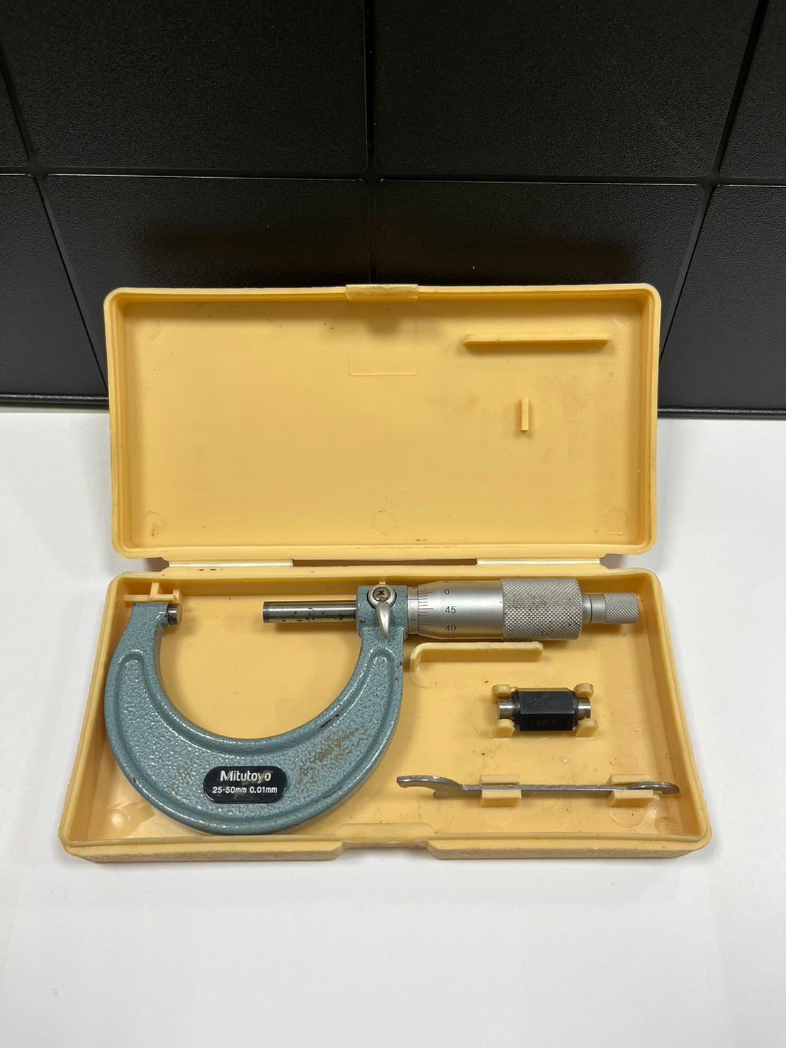 A micrometer is sitting in a yellow case on a table.