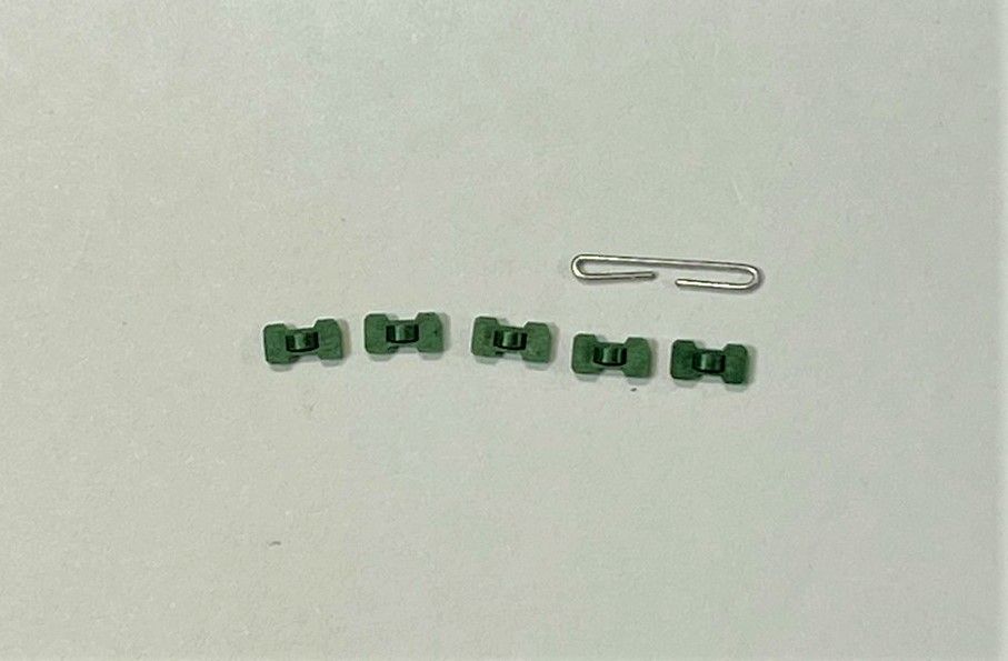 A group of green buttons and a paper clip on a white surface.