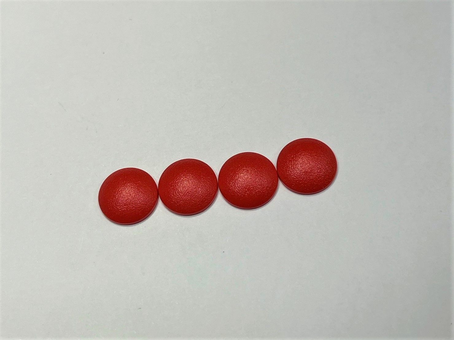 Four red buttons are lined up in a row on a white surface.