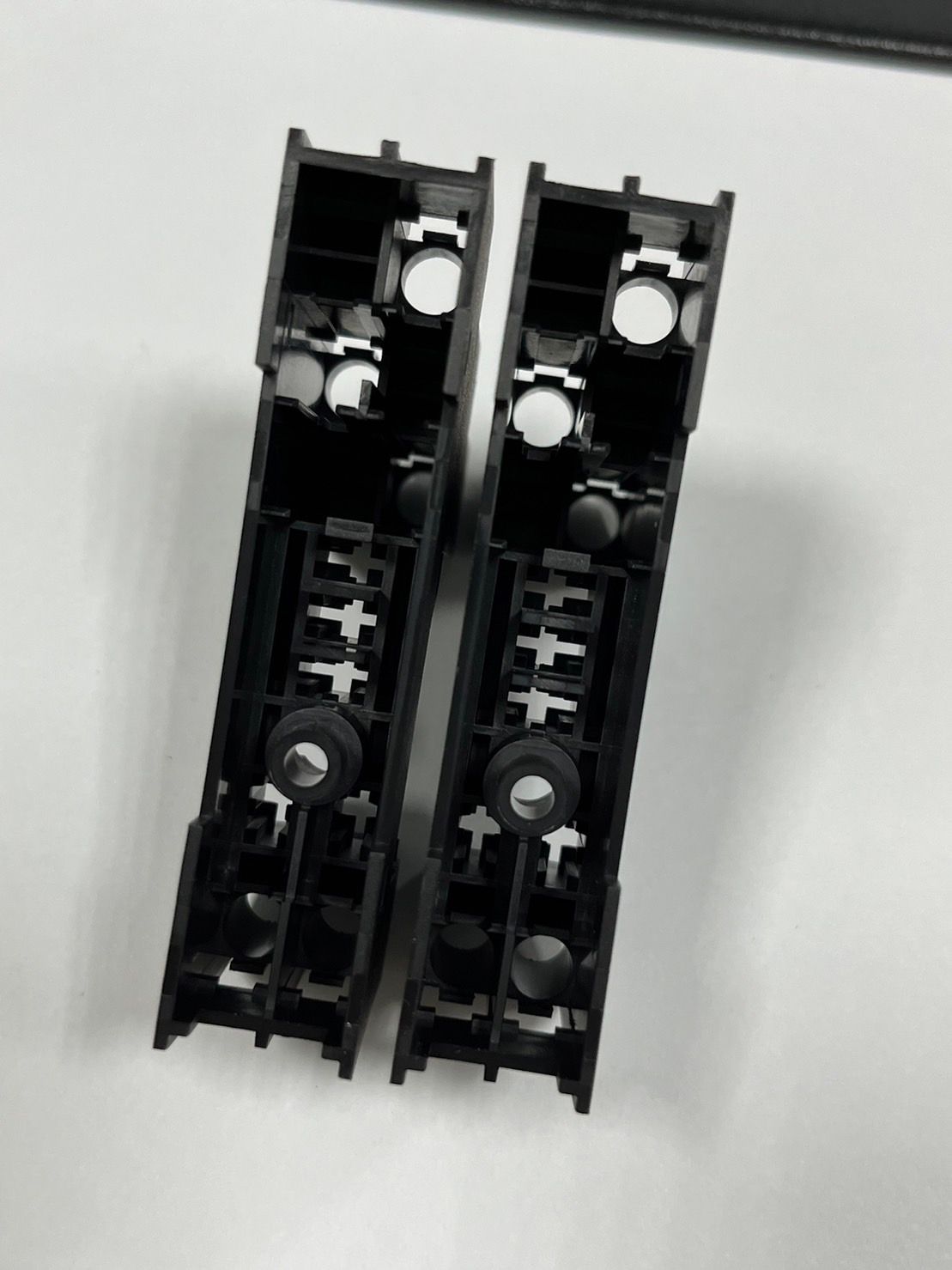 Two black plastic pieces are sitting on a white surface.