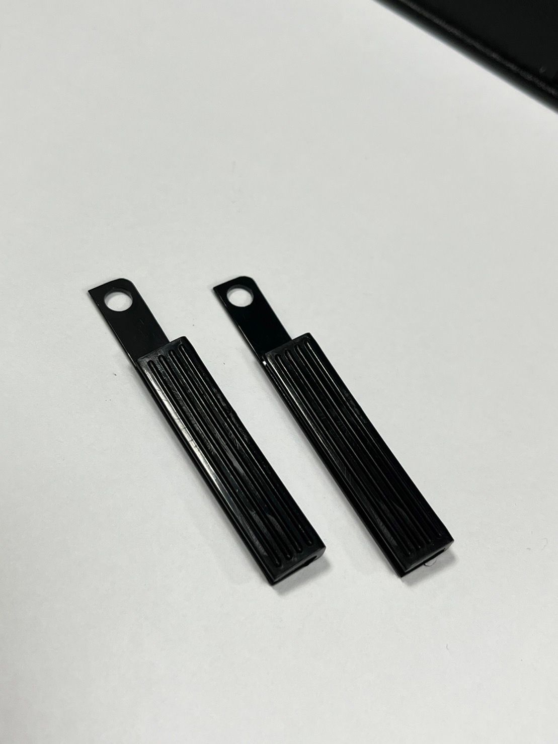 Two black sticks with holes in them are sitting on a white surface.