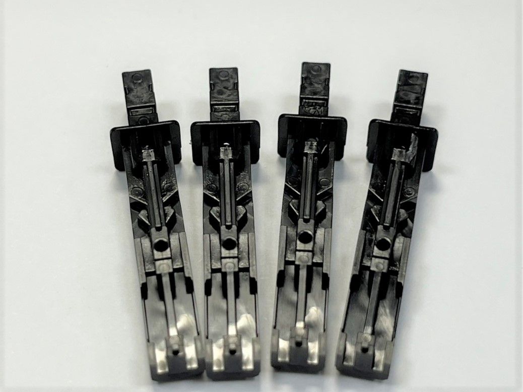 Four black plastic clips are sitting on top of each other on a white surface.