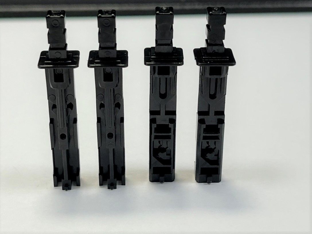 Four black pieces of plastic are lined up on a white surface
