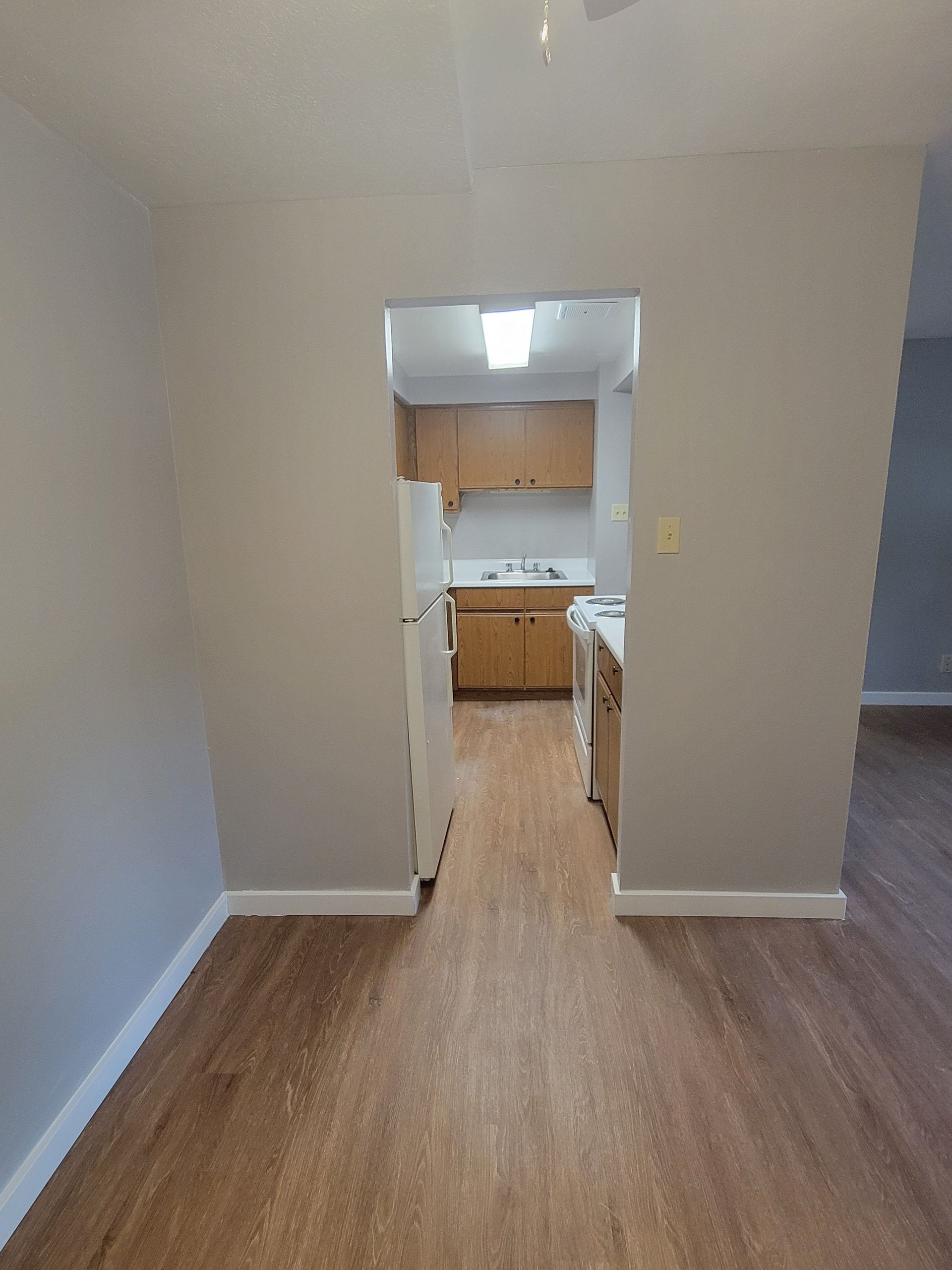 A kitchen with a refrigerator , stove , sink , cabinets and hardwood floors.
