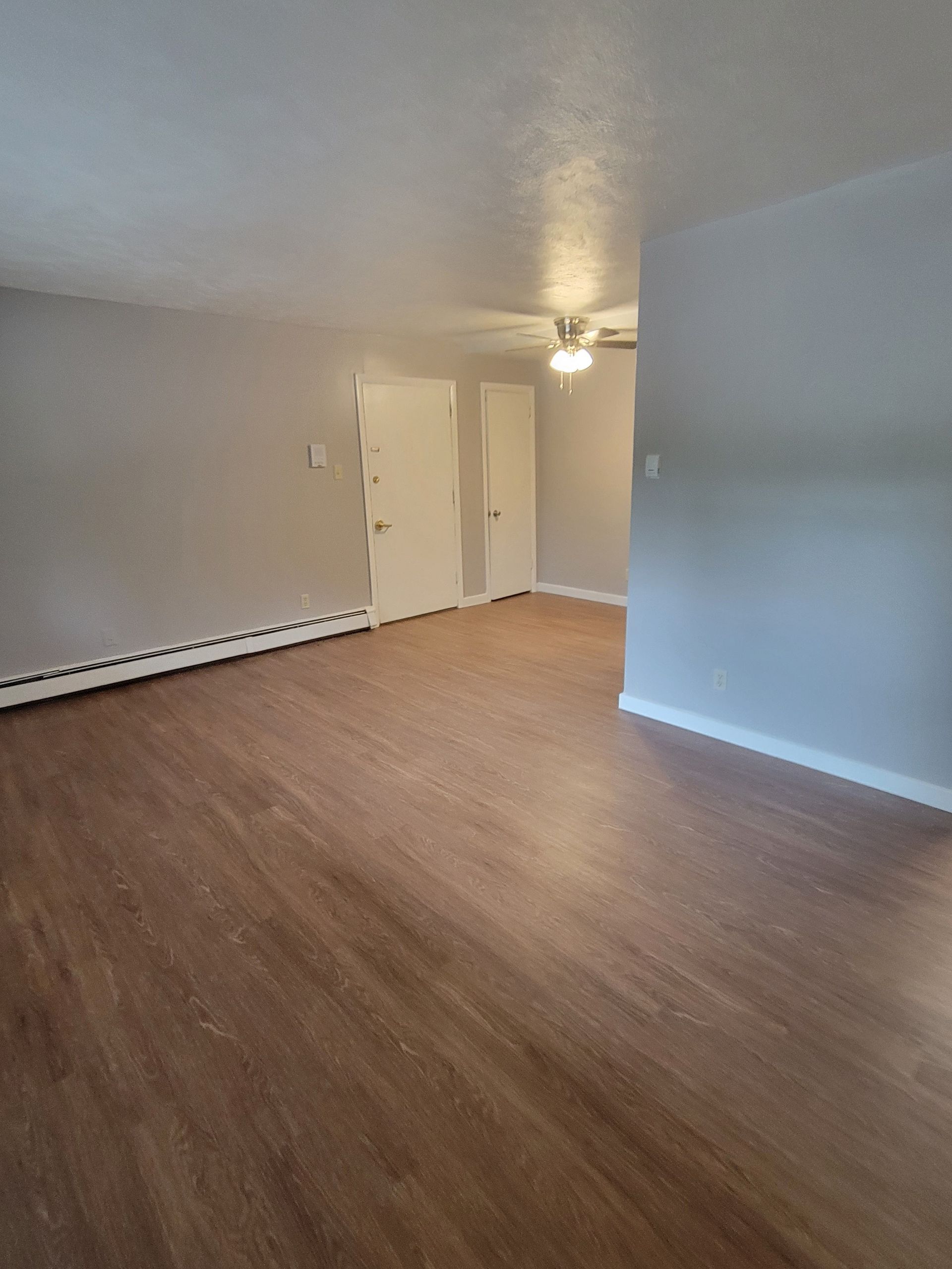 An empty living room with hardwood floors and a ceiling fan.