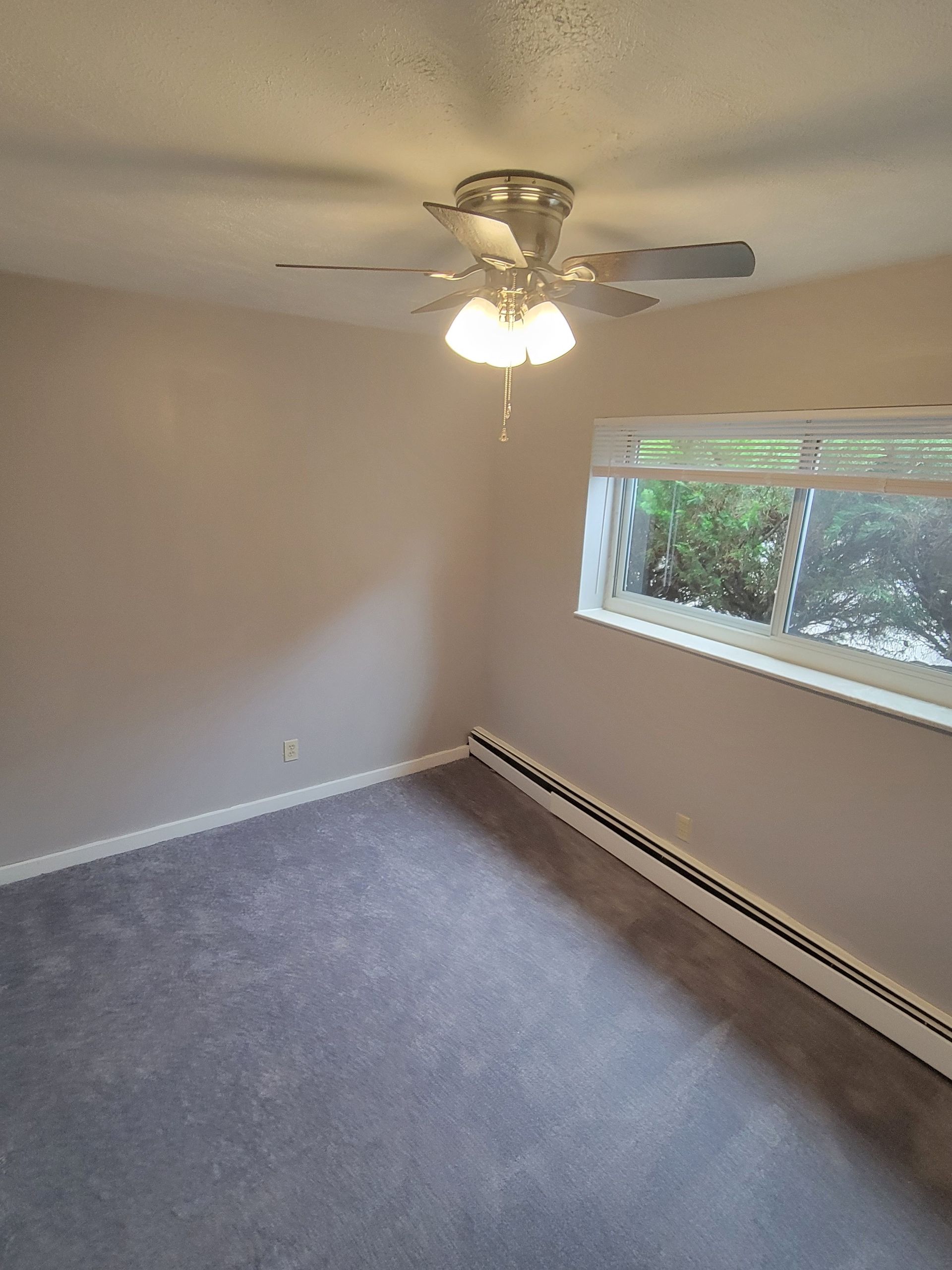 An empty bedroom with a ceiling fan and a window.