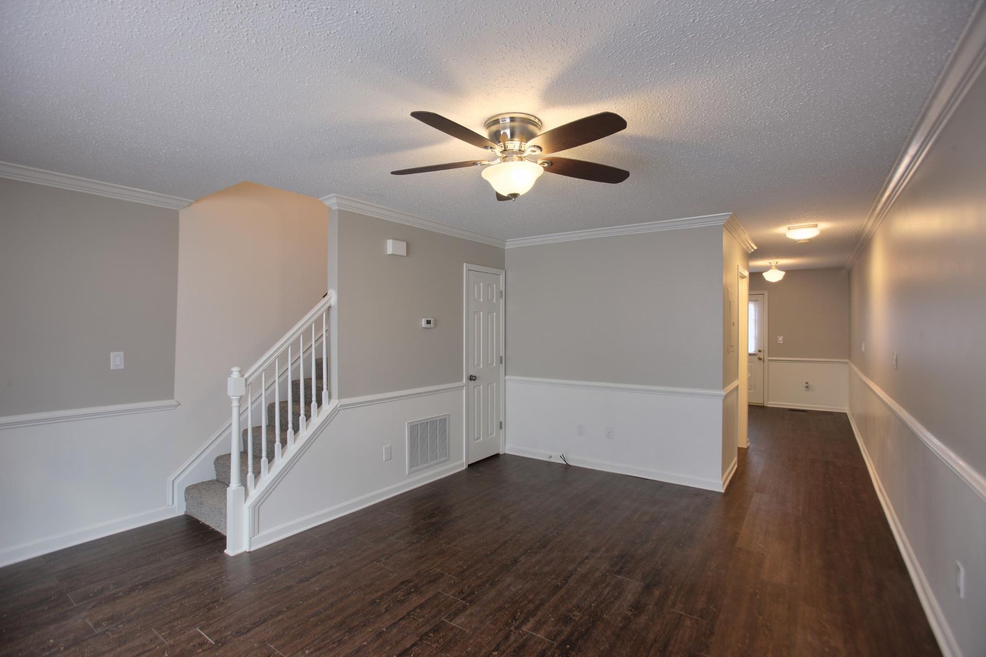 Living room with staircase, ceiling fan, and dark wood floor. 