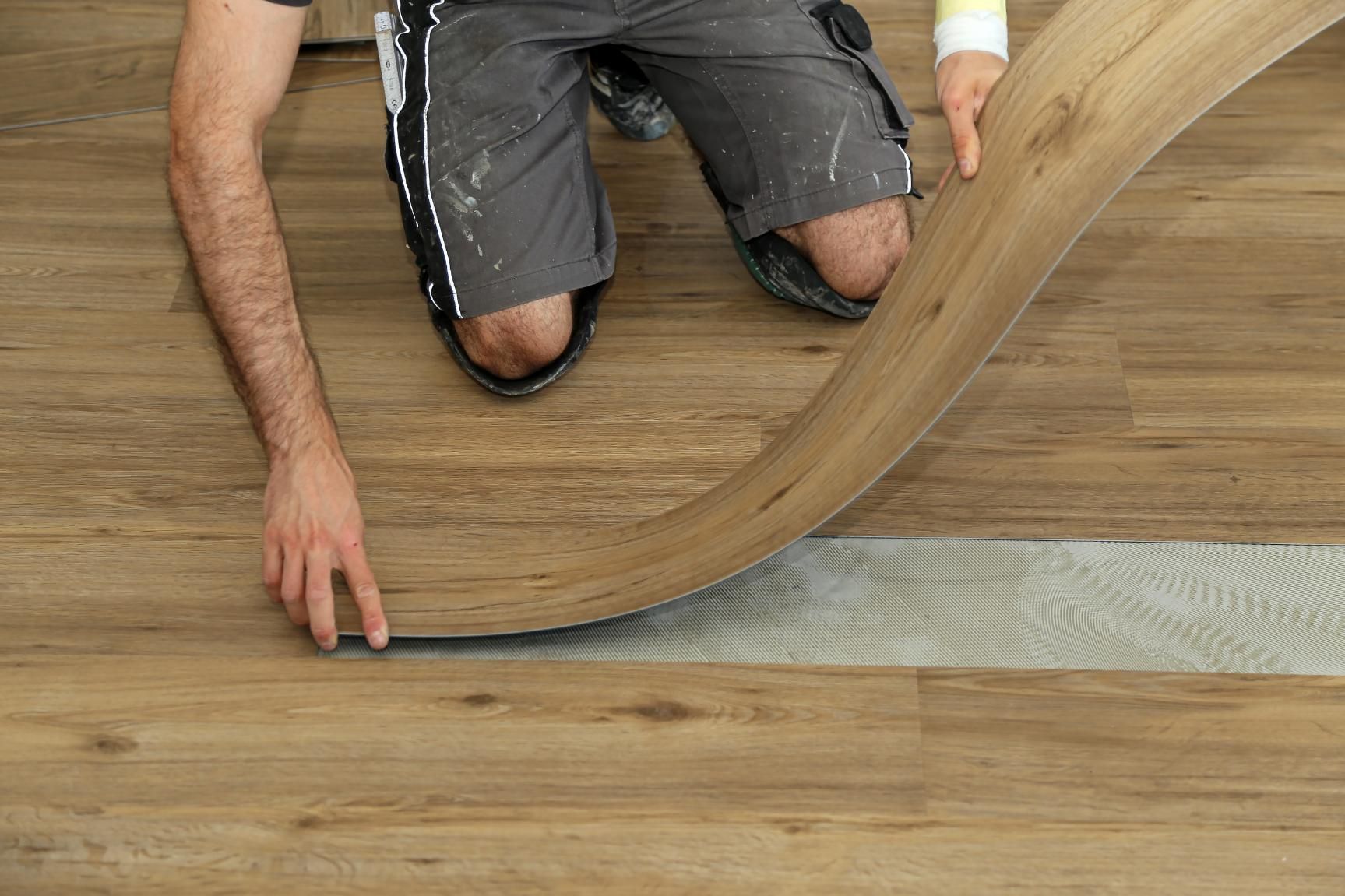 Person installing wood-look flooring, kneeling. 