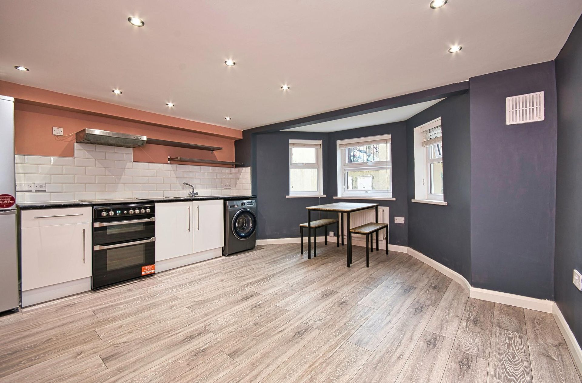 Open-plan kitchen and dining area with wood floors, white cabinets, and navy walls.