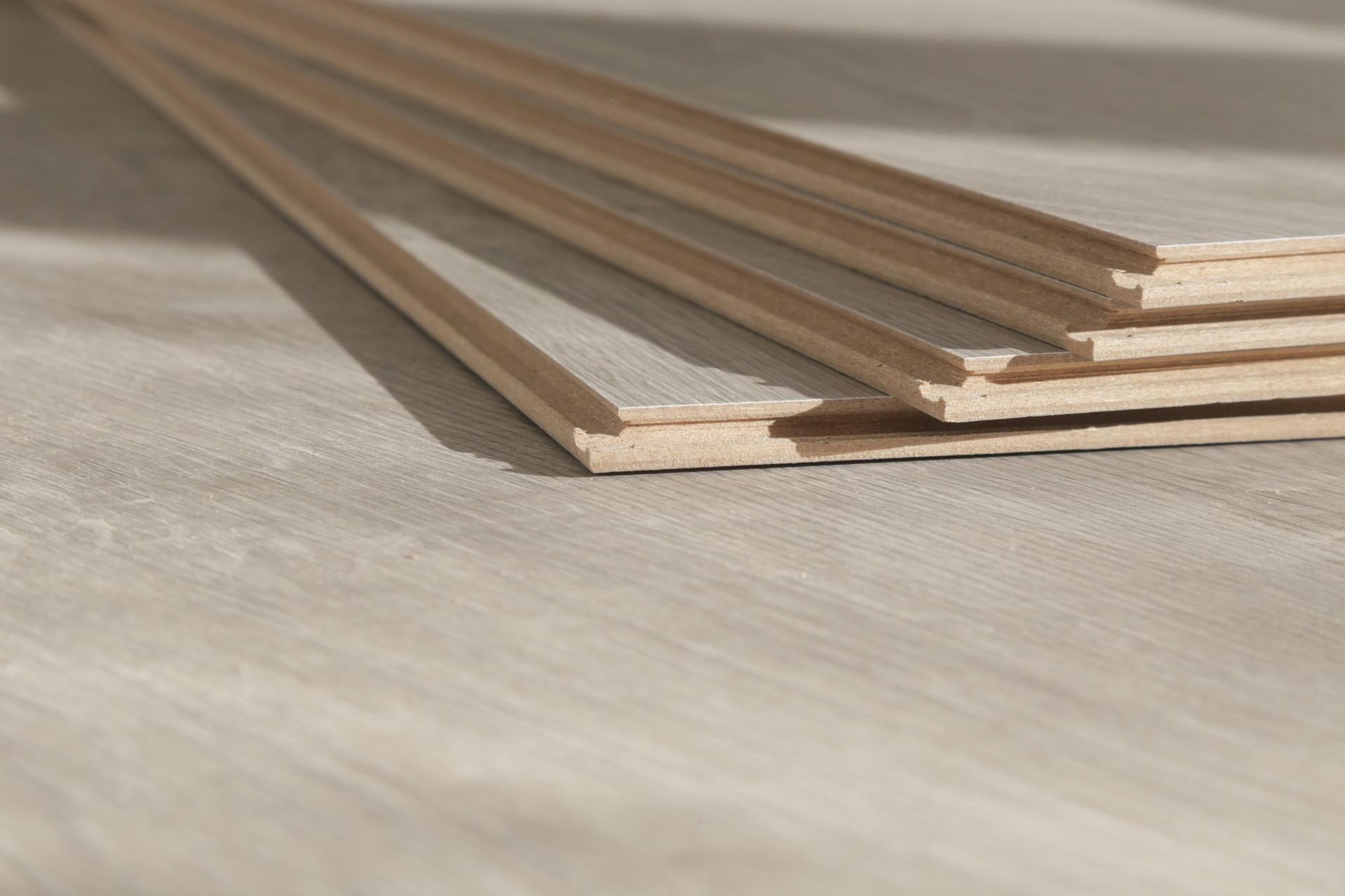 Light-colored wood flooring planks, stacked and angled on a textured surface.