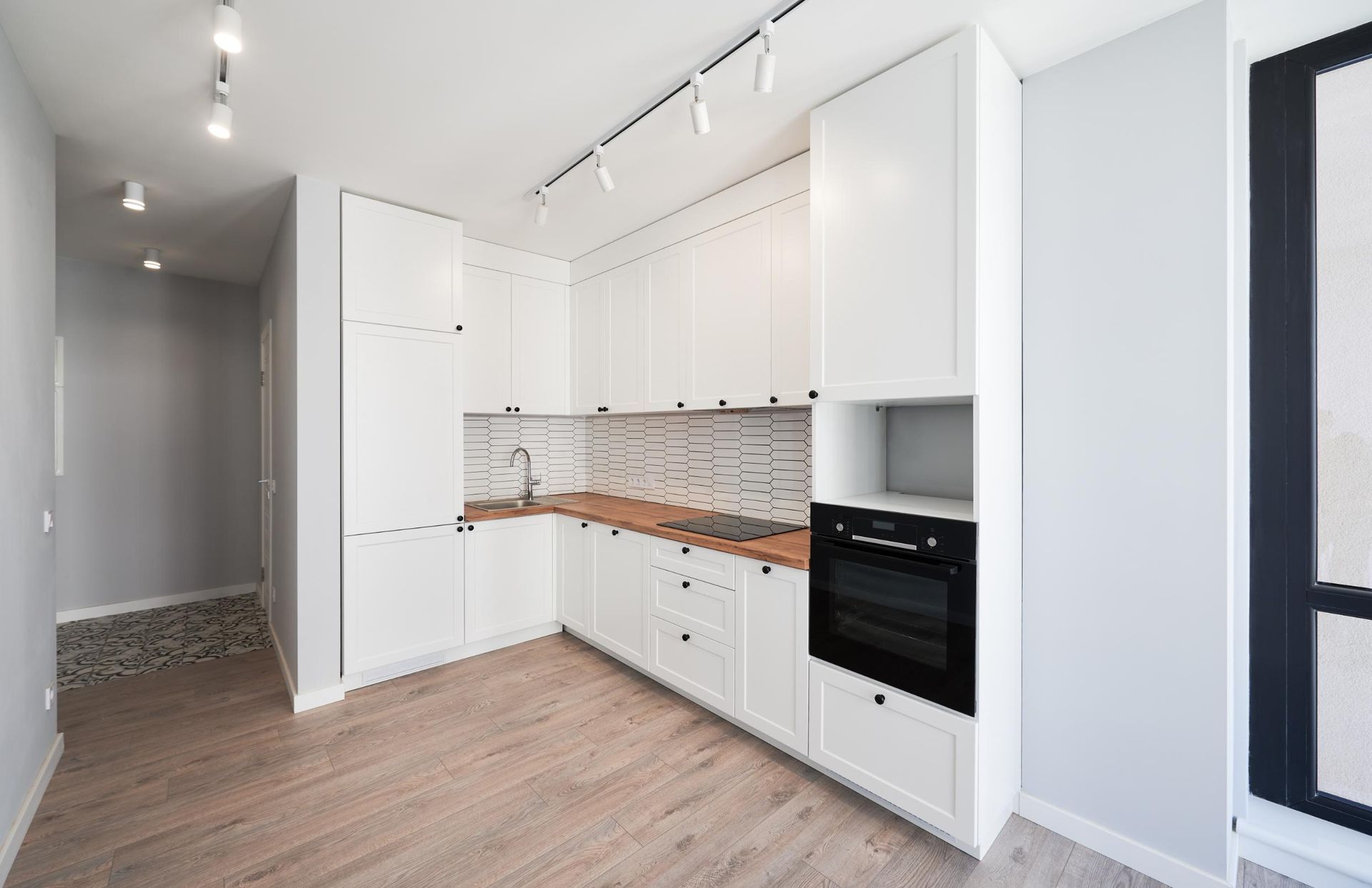 Modern white kitchen with wood countertops, a black oven, and track lighting.