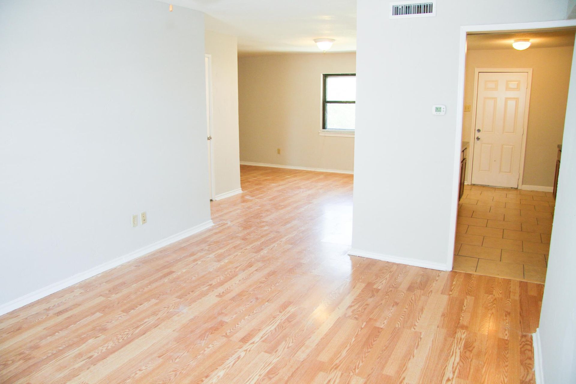 Empty living room with wood floors and white walls; doorway to hallway with exterior door.