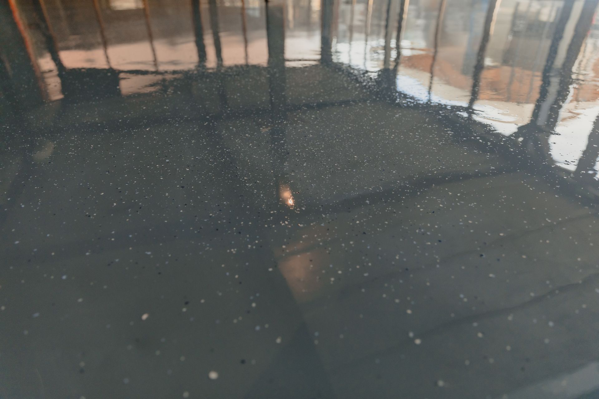 Dark gray, reflective surface speckled with white, reflecting a building.