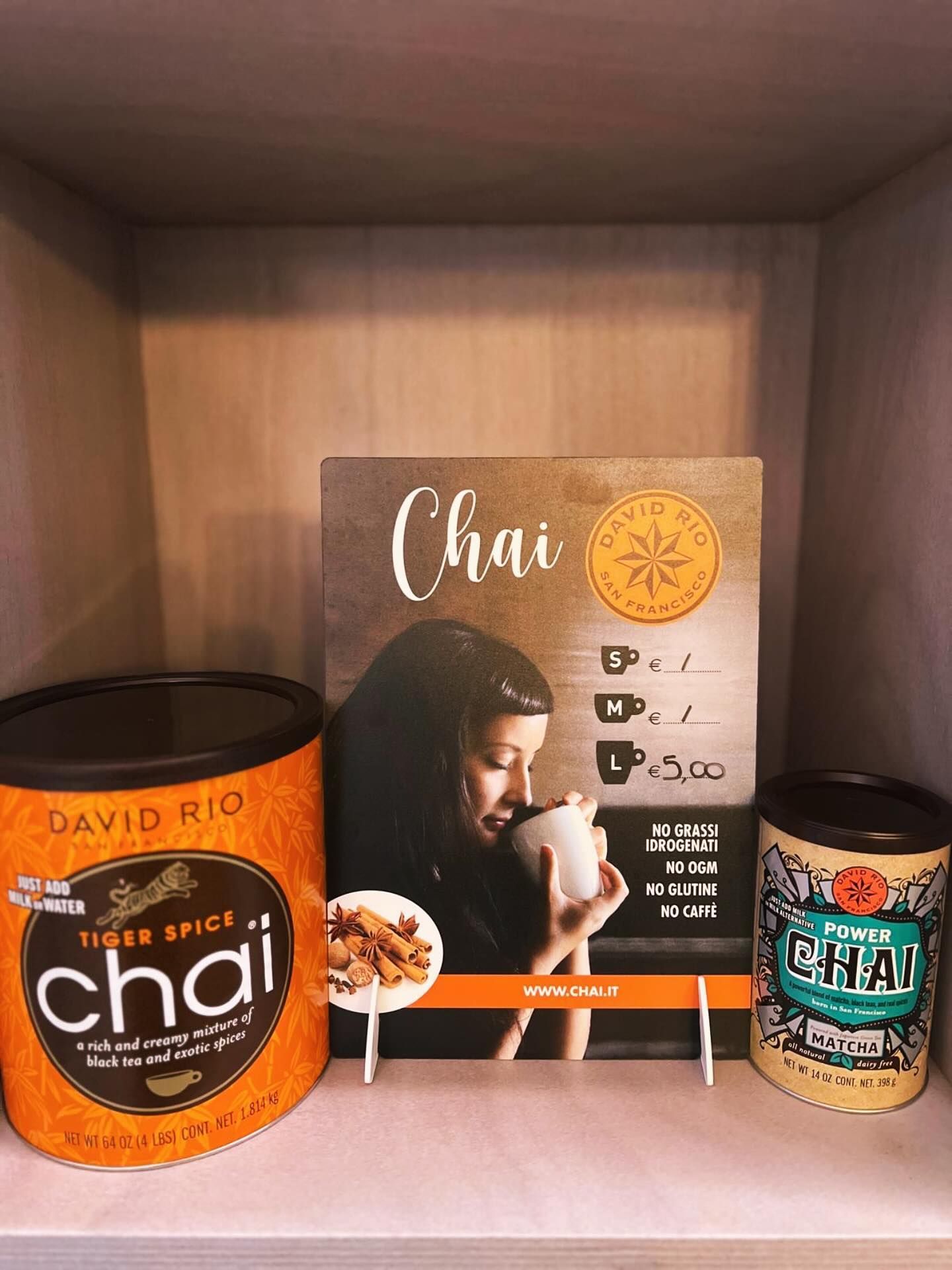 Un espositore di tè chai David Rio con un grande barattolo di Tiger Spice, un listino prezzi e un barattolo più piccolo di Power Chai su uno scaffale.